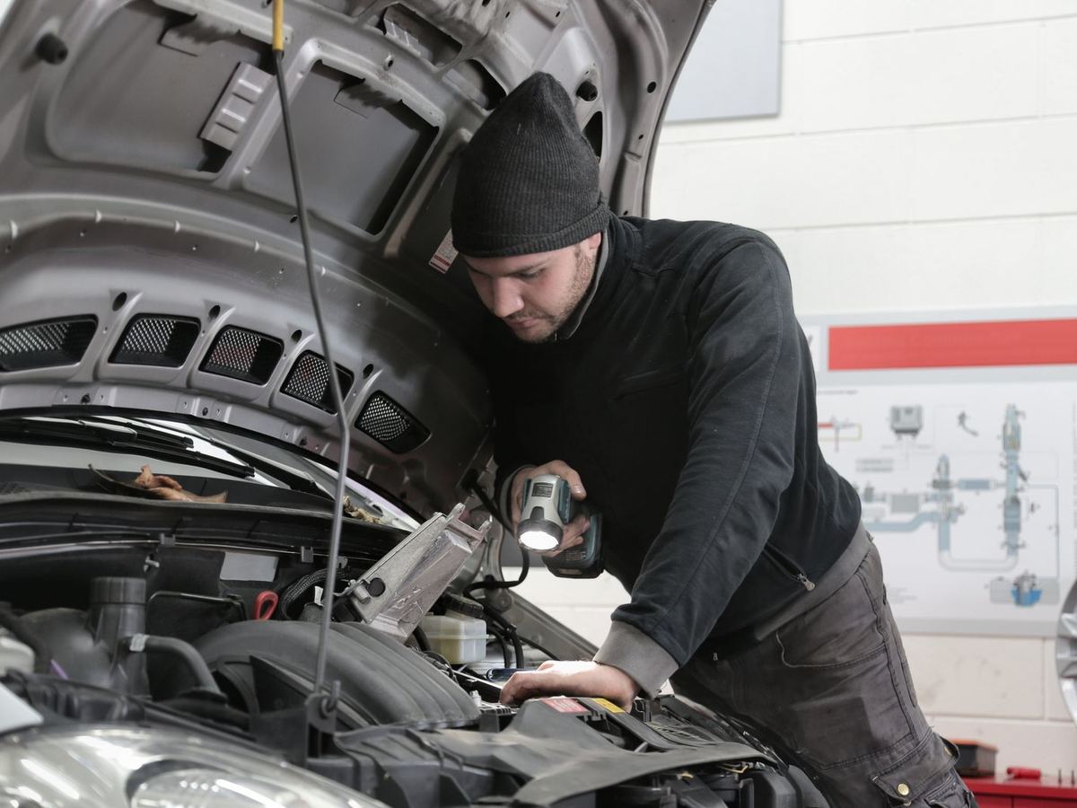 Stock photo: a mechanic shining a work light into the engine bay of an ordinary car.