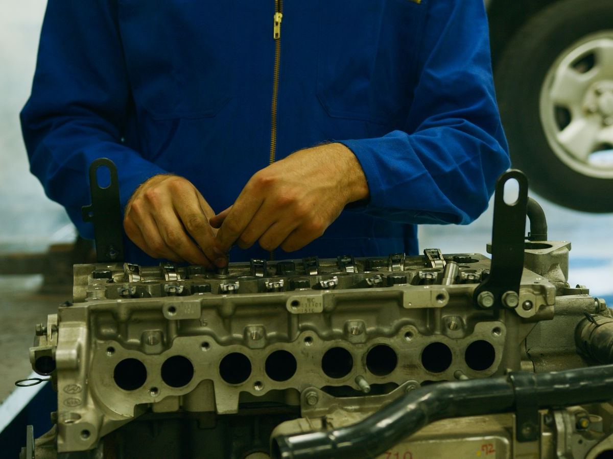 Stock photo: gloved hands working on a bare engine block on a stand in a workshop.
