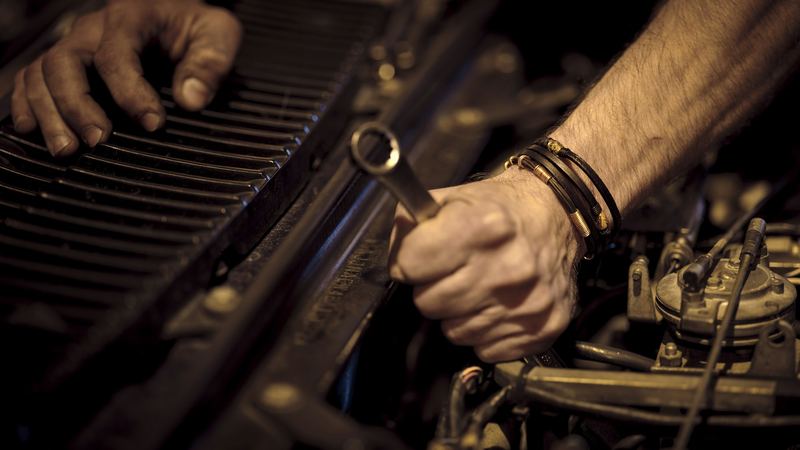 Hands using a wrench on a car engine. Stock photo.