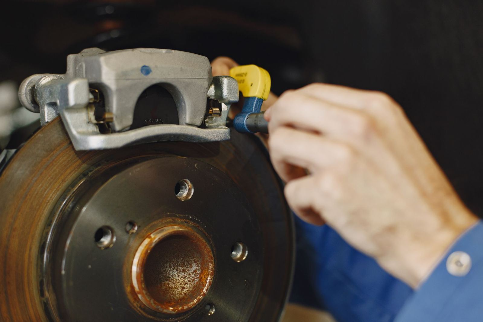 A hand working on a brake caliper mounted over a rotor. Stock photograph.