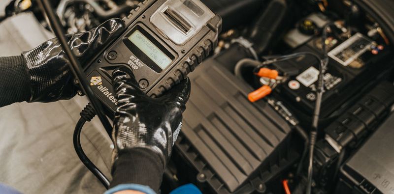 A gloved hand holding a scan tool over the open engine bay of an ordinary car. Stock photograph.