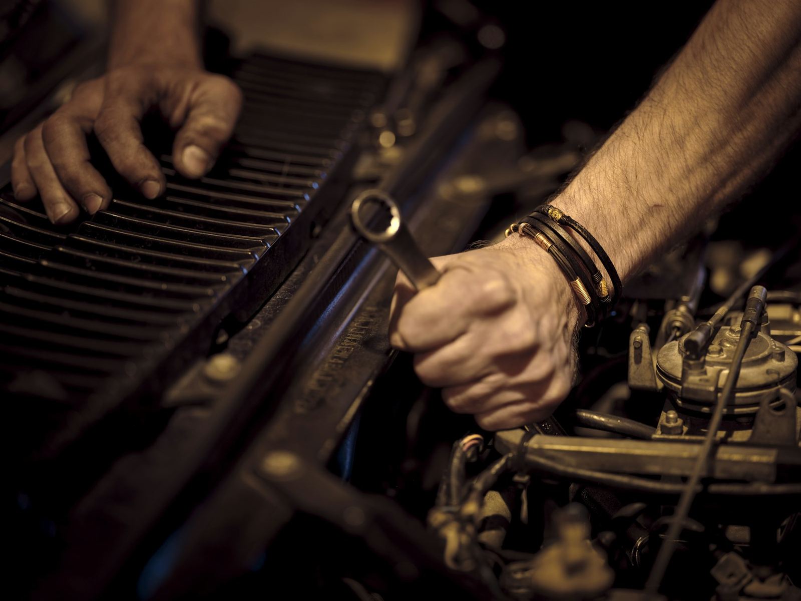 Two hands working with a wrench inside an engine bay. Stock photograph.